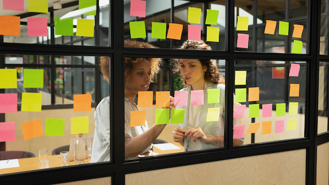 Two woman looking at sticking notes on a glass wall