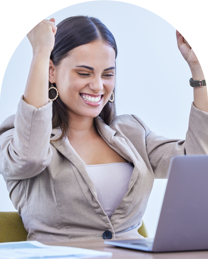 Happy woman seated at laptop with hands raised in victory